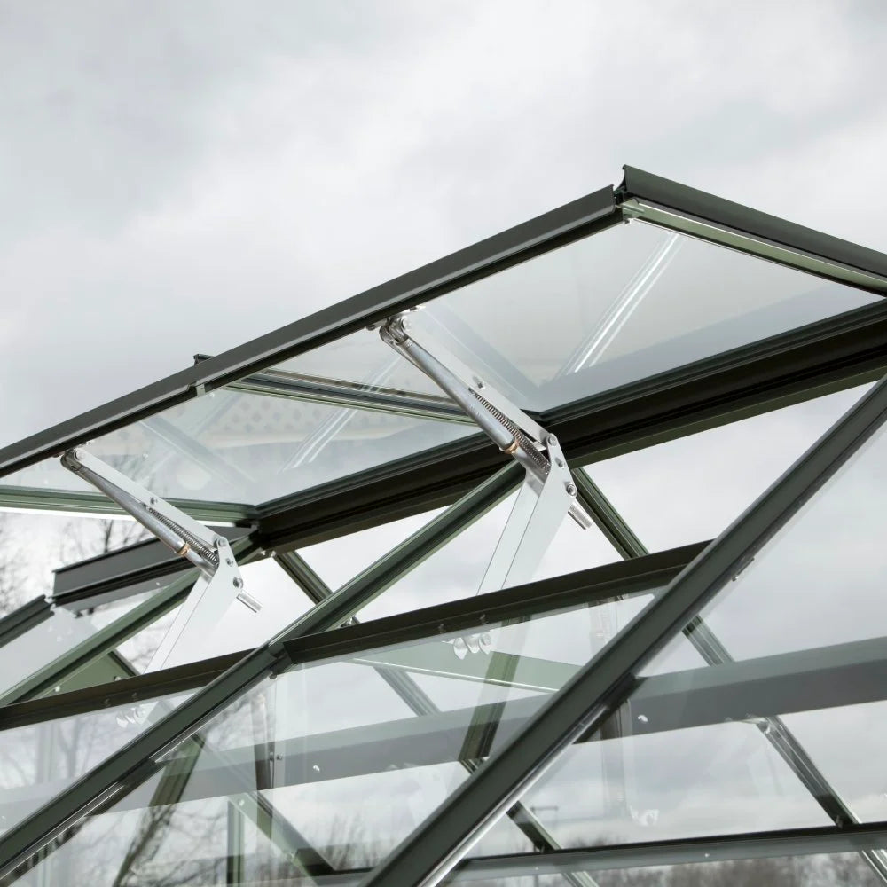 Glass Rhino Greenhouse roof with vent panels slightly open, supported by metal arms; set against a cloudy sky.