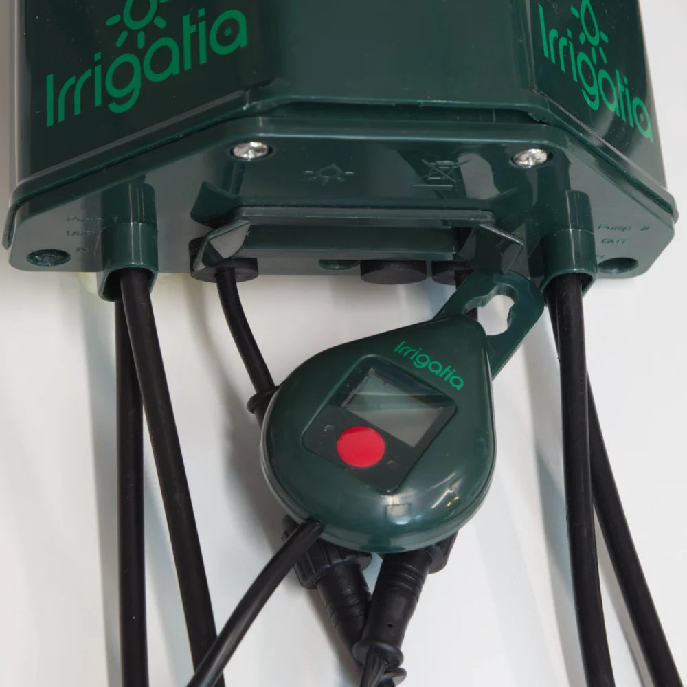 A green irrigation system labeled Irrigatia is shown, featuring multiple attached tubes, a digital display, and a red button. It is set against a plain background.