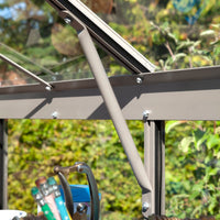 Metal support rod secures Rhino Greenhouse window, surrounded by gardening tools in a sunlit, leafy environment.