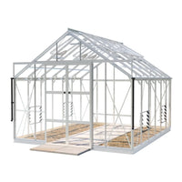 A white, metal-framed Rhino Greenhouse with clear panels and open double doors stands on a concrete base. The interior shows orderly soil paths, and it appears to be in an outdoor setting.