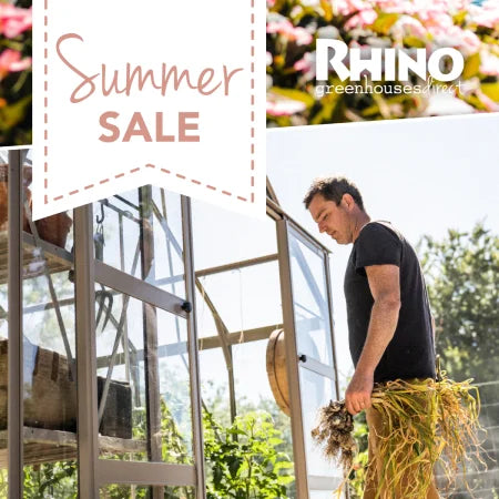 A person holds freshly harvested plants near a glass Rhino Greenhouse under a clear sky. Two text elements read: Summer Sale and RHINO Rhino Greenhouses direct in the upper corners.