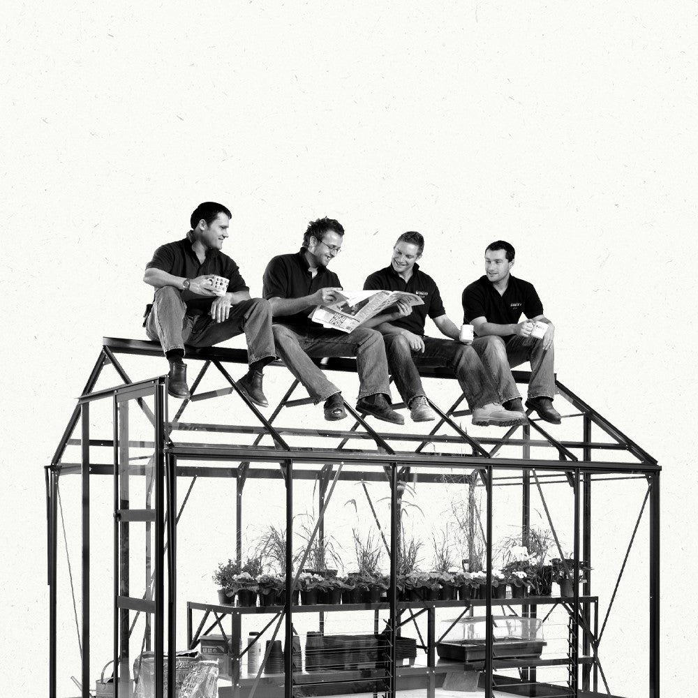 Four men sit atop a Rhino Greenhouse frame, engaging in conversation and reading a newspaper. Below, plants are arranged in pots on shelves, suggesting a gardening context.