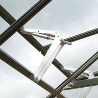 A metal window hinge mechanism opens a glass panel in a Rhino Greenhouse. The overcast sky is visible through the glass panes, emphasizing the outdoor environment.