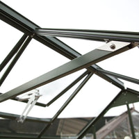 A dark green metal Rhino Greenhouse frame is shown from below, with connected beams and bolts, set against an overcast sky.