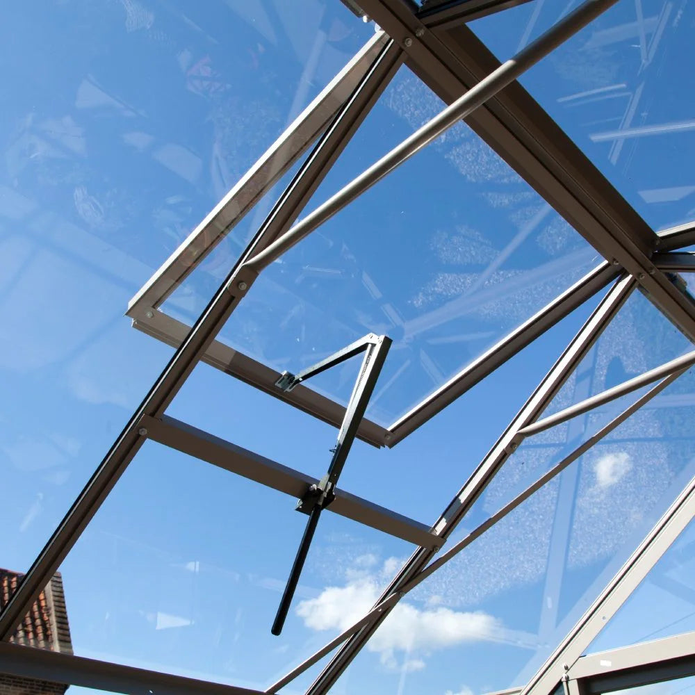 Open Rhino Greenhouse window with brown metal frame tilting upwards under a clear blue sky, showing white clouds in the background.