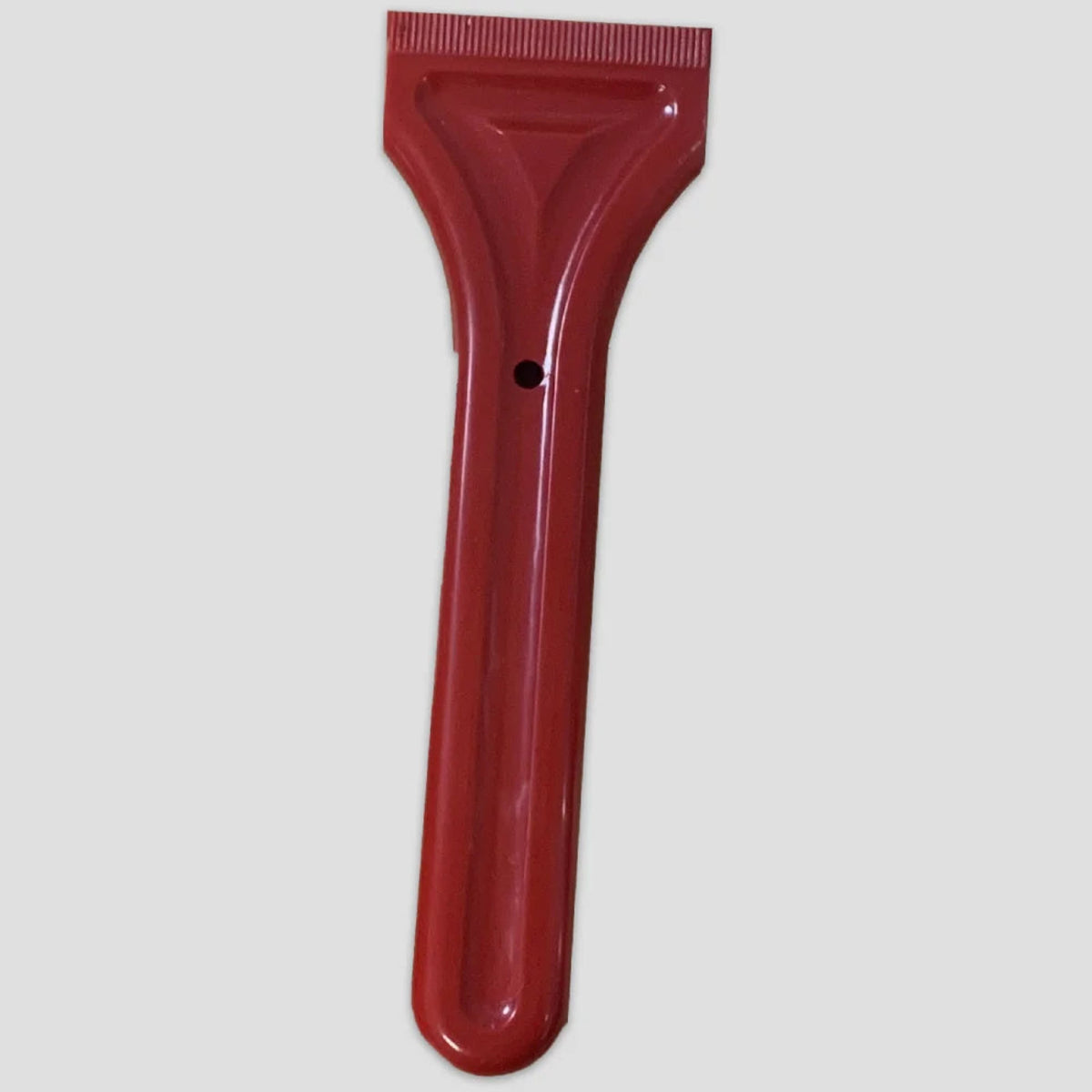 Red plastic scraper with a flat, ridged edge and long handle featuring a hole for hanging; set against a neutral gray background.