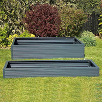 Two rectangular, metal garden planters rest on a grassy lawn. The background features lush greenery, including various shrubs and trees, creating a garden setting.